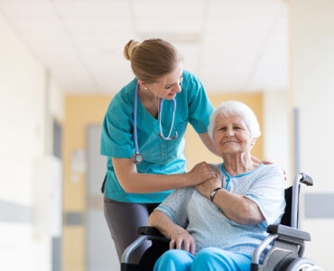 Starsza kobieta po udarze siedzi na wózku i rozmawia z pielęgniarką