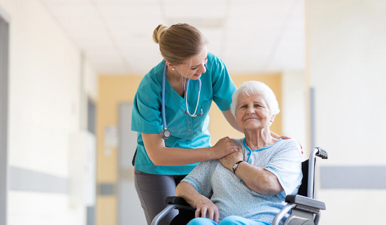 Starsza kobieta po udarze siedzi na wózku i rozmawia z pielęgniarką