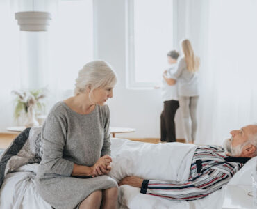 Kobieta opiekuje się starszym mężczyzną który leży w łóżku rehabilitacyjnym